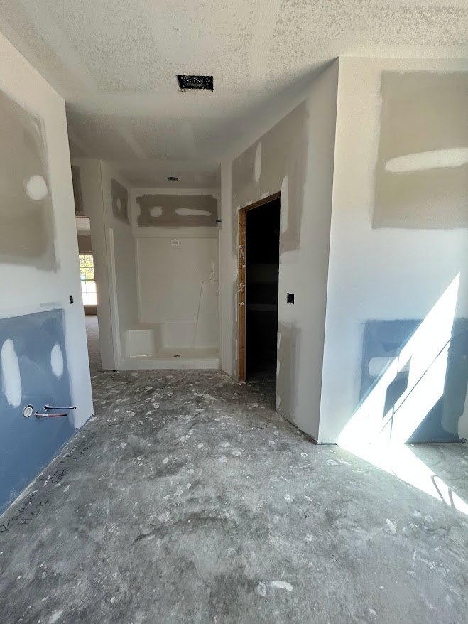 Bathroom with concrete floor, blue accent wall, white walls, glass shower enclosure, and wooden door