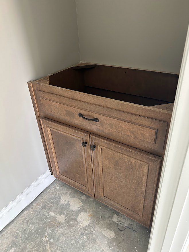 Wood cabinet with drawers and cupboard doors set against a light-colored wall, hardwood floor visible in foreground.