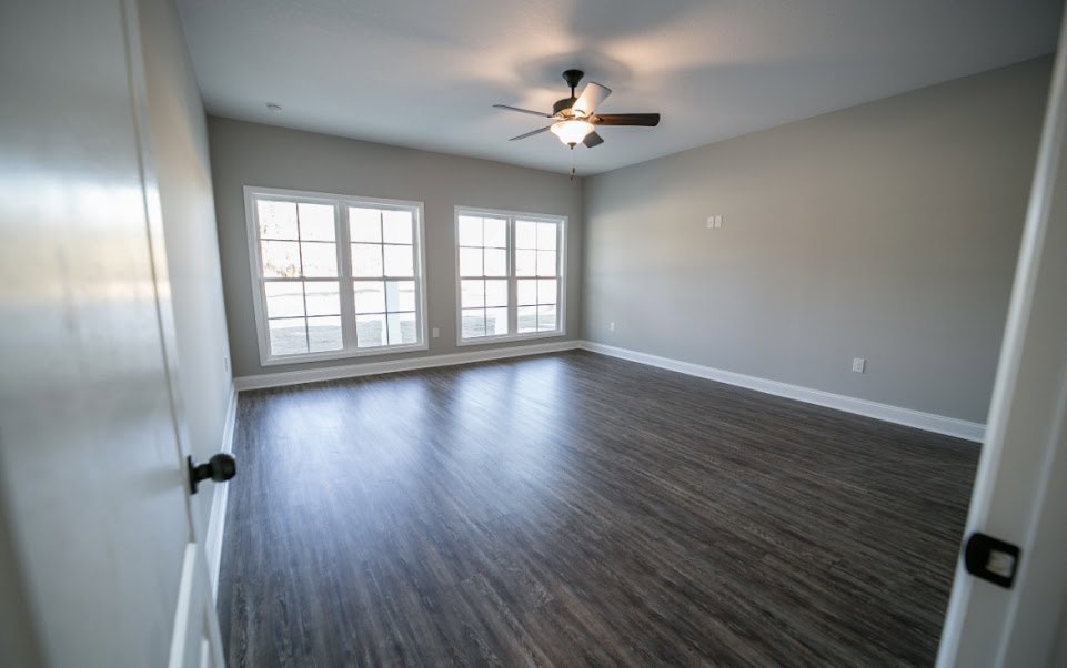 Ceiling fan with light fixture above wood laminate flooring, row of multi-pane windows along white wall in residential interior.