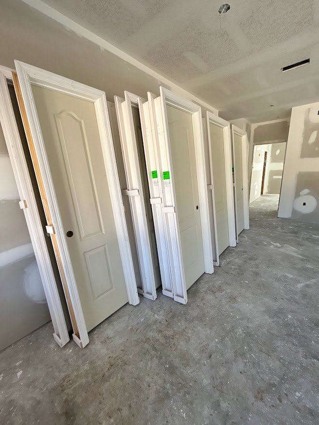 Row of white interior doors along a plaster wall, green signs on one door, light flooring and ceiling visible