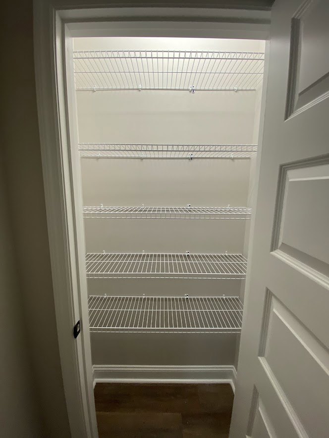 White closet with built-in shelves, wood flooring, and a closed door with a metal handle