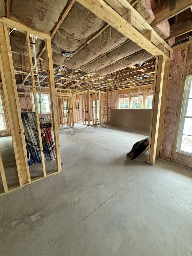 Open room with exposed wood ceiling beams, unfinished walls, bags of insulation material, and shelving with construction supplies