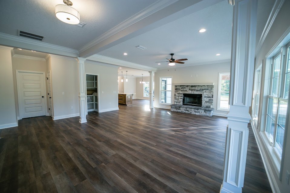Spacious living area with hardwood flooring, white walls, central fireplace with white mantel, white door featuring black knob, ceiling light fixture with white shade, and large