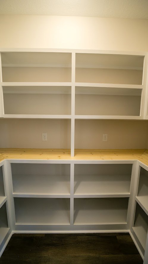 White built-in shelves against a light-colored wall in an empty room with hardwood flooring