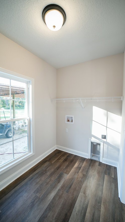 Wood-floored room featuring a large window, white plaster walls, and a close-up of a blue upholstered chair