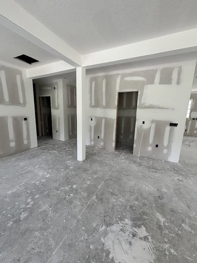 White-walled room with painted concrete floor, white pillars, and a close-up view of a grey door surface; white object casting a shadow against the wall.