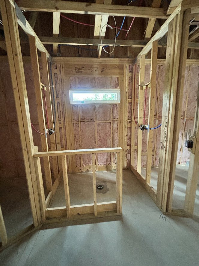 Unfinished room with exposed wooden beams, plywood flooring, and a large window framed by insulation