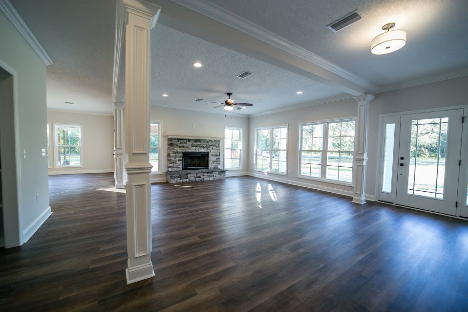 Spacious living area with hardwood floors, central stone fireplace, multi-pane windows, ceiling light fixture, and white glass-paneled door