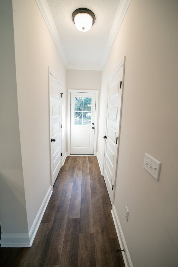 Hallway with white paneled doors, dark wood laminate flooring, smooth plaster walls, and recessed ceiling lights
