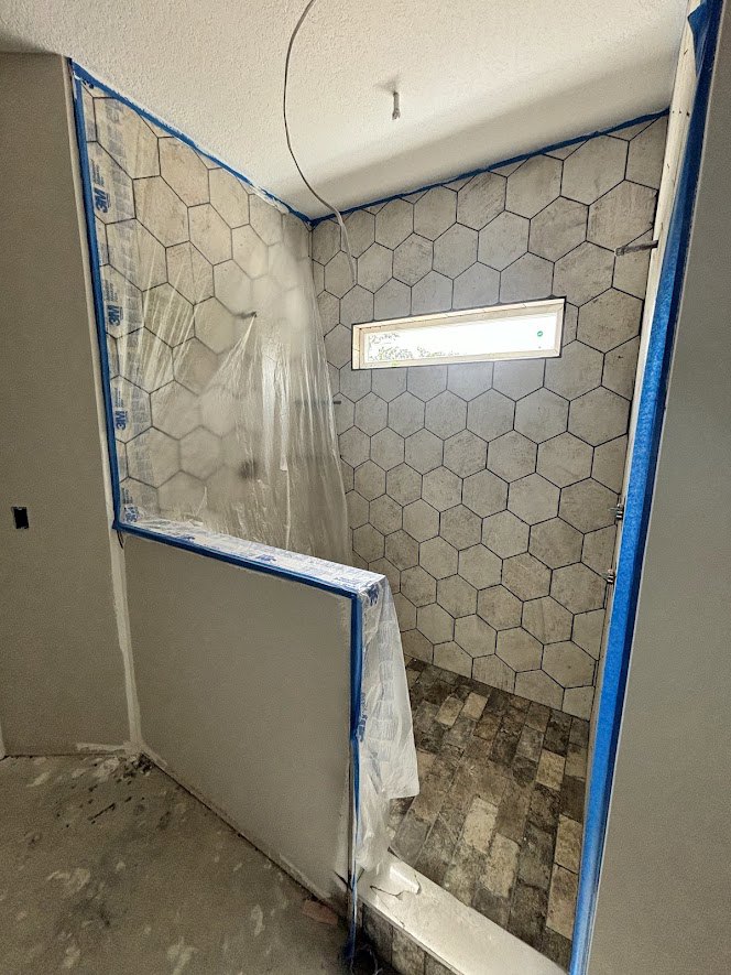 Bathroom with gray tile wall and matching tile floor, window with frosted glass, recessed ceiling light, white plaster ceiling, minimalist fixtures