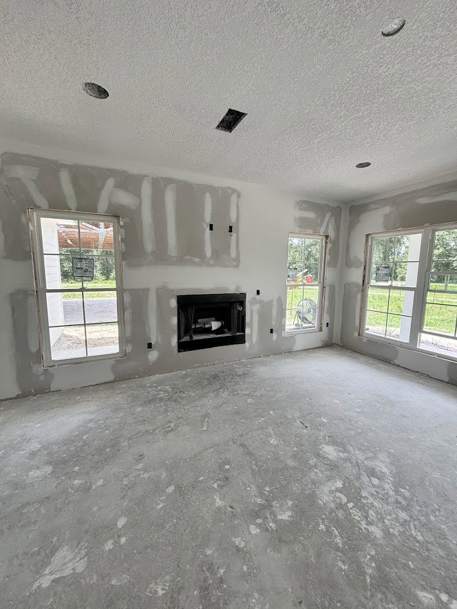 Living room with plaster walls, large windows overlooking yard, concrete floor, built-in fireplace, and vented ceiling