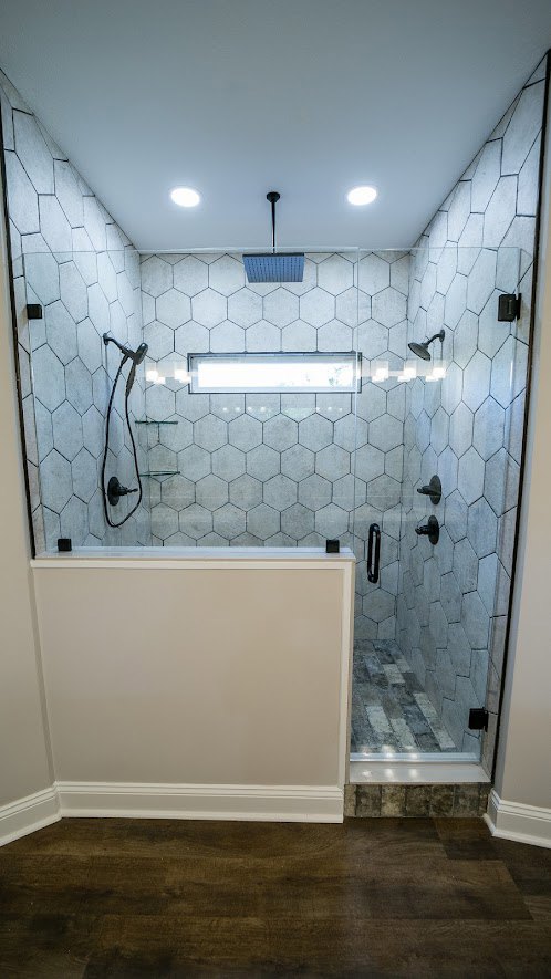 Walk-in shower with clear glass door, white tile walls, chrome fixtures, and light gray floor tiles