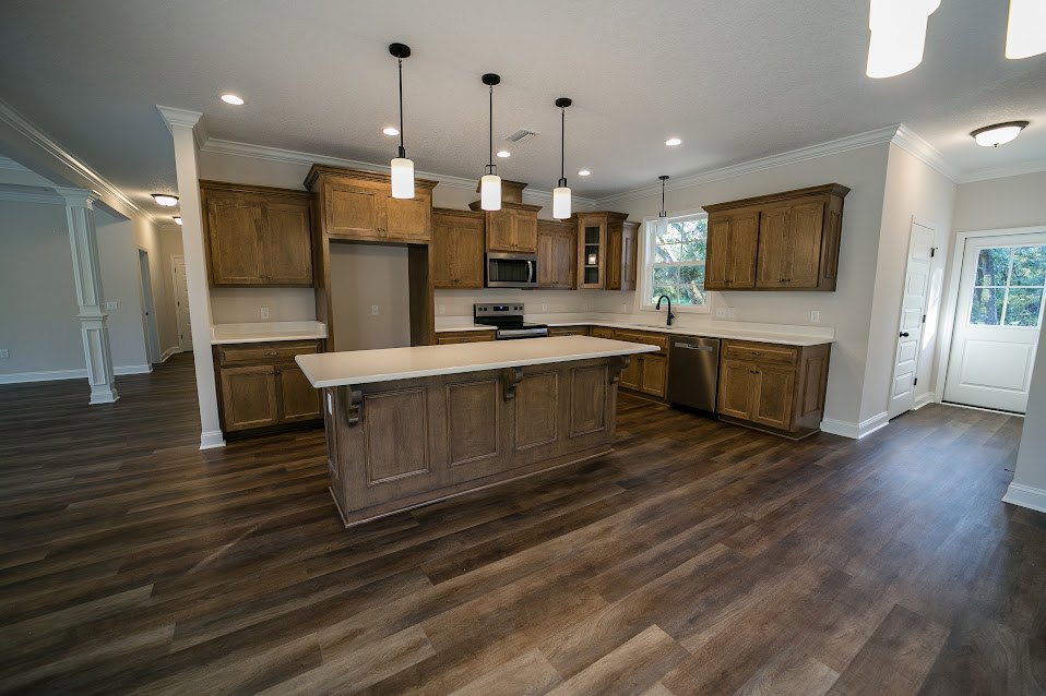 Kitchen with natural wood cabinets, matching hardwood floor, silver refrigerator, white door with window, and light-colored countertop.