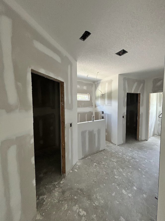 Room with smooth white plaster walls, white ceiling, concrete floor painted white, and a single white door.