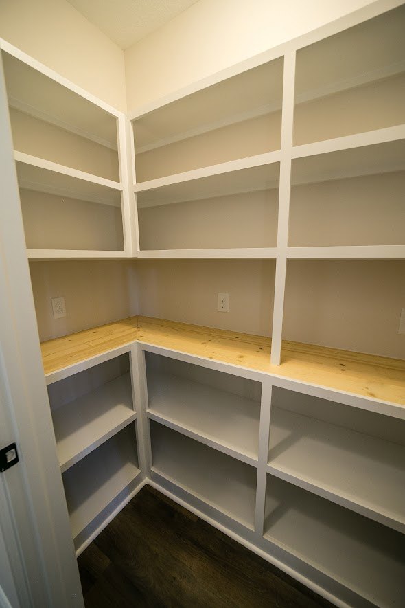Walk-in closet featuring multiple white built-in shelves, wood flooring, and a white door, with empty shelving units lining the walls.