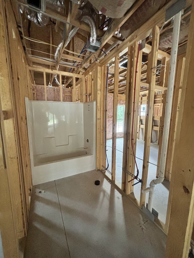 Bathroom under construction featuring exposed wood beams, unfinished plaster walls, visible plumbing pipes, and a framed shower enclosure.