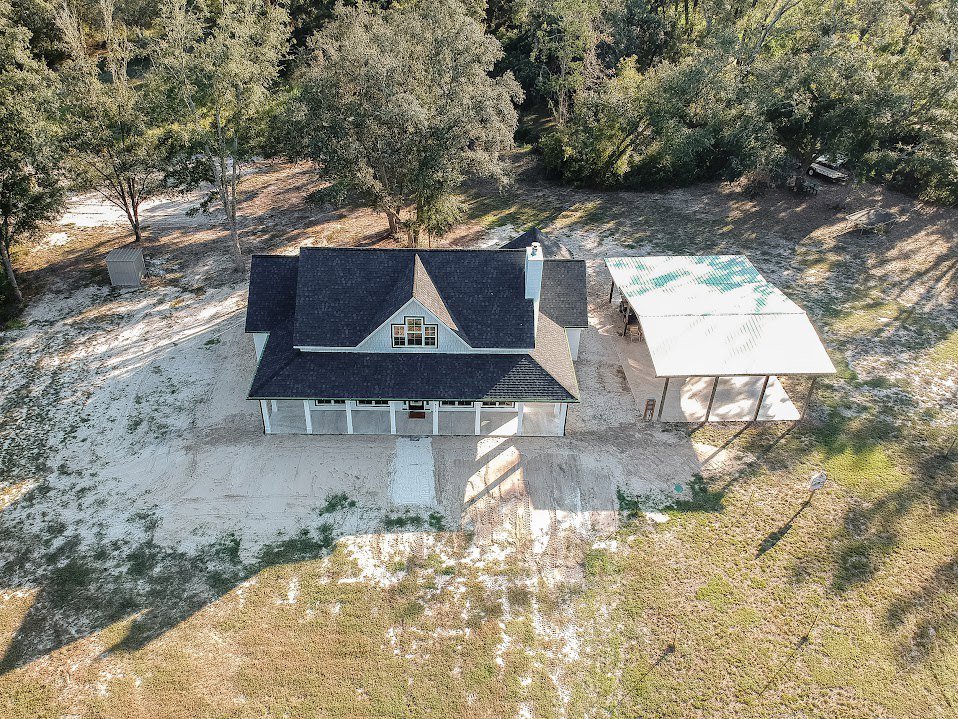 Covered front porch with white roof, surrounded by mature trees and green grass