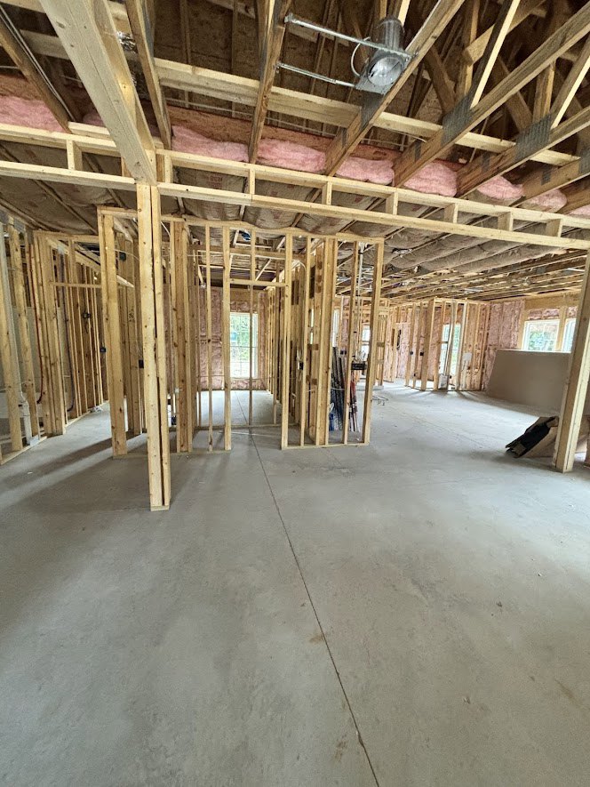 Exposed wood beams and framing with metal ceiling fan, window, and unfinished floor in a custom home interior