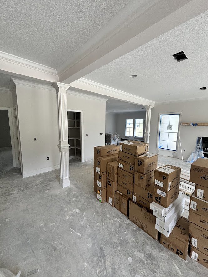 Stacked moving boxes fill a room with light-colored walls, a white shelving unit, and a rectangular window with a blue accent strip.
