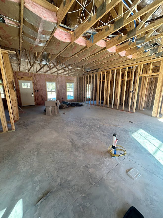 Concrete floor with yellow hose, exposed wooden ceiling beams with insulation, white door featuring window, visible metal tubing along ceiling and floor.