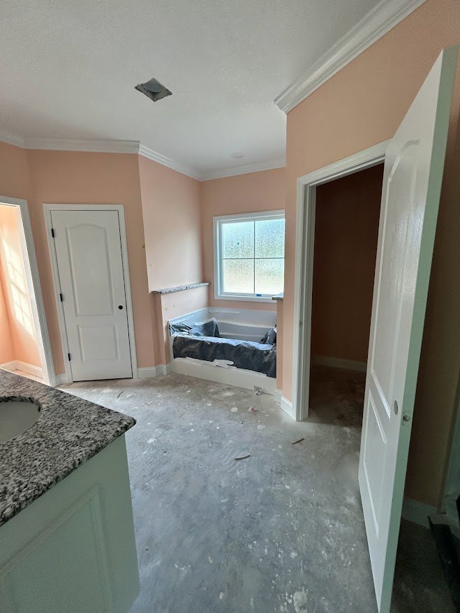 Bathroom with freestanding tub filled with foam, white countertop sink, frosted glass window, white door with black knobs, plaster walls, and light flooring.