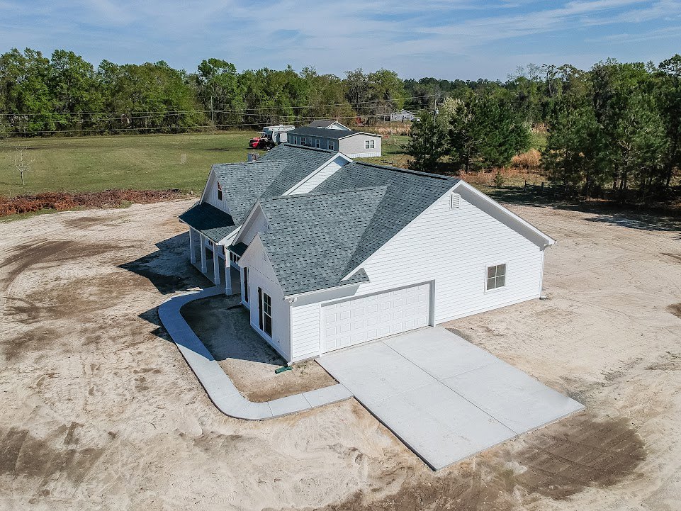 Two-story home with gray shingle roof, attached garage, concrete driveway, manicured lawn, and blue sky with scattered clouds