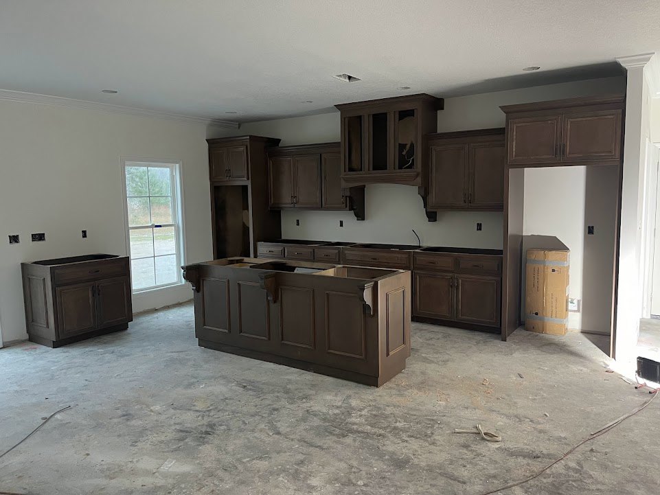 Dark wood kitchen cabinets beneath a white ceiling, white-framed window above the sink, glass-front cupboards, light countertops, and stainless steel appliances.