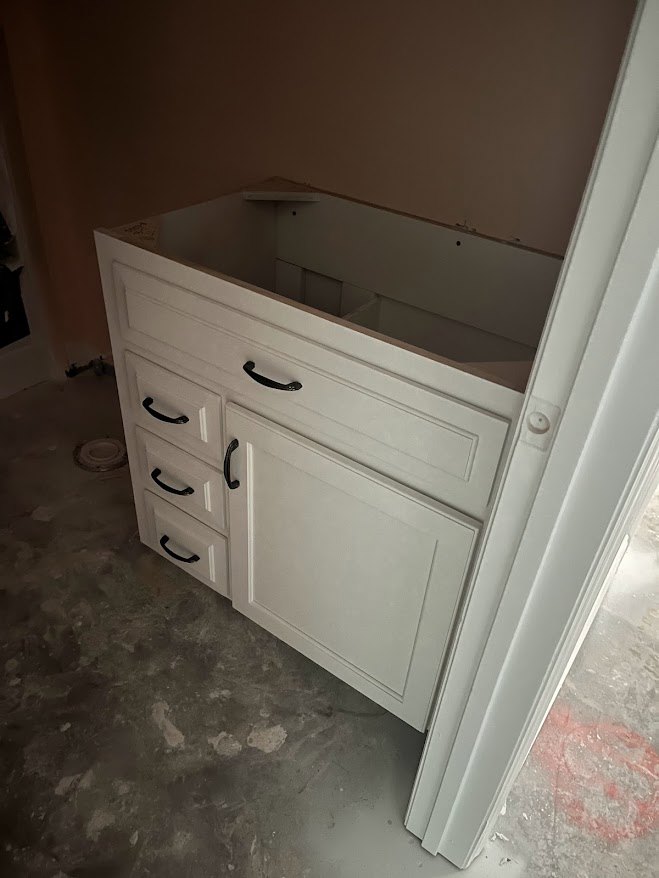 White cabinet with multiple drawers, matte black handles, and smooth white finish, set against a light-colored wall and floor.