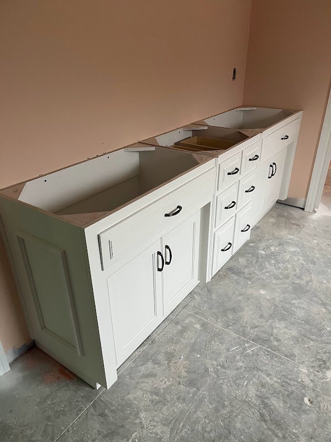 White quartz countertop with built-in drawers, white cabinetry, brown storage box on open shelf, grey tile flooring with white base trim, stainless steel sink and faucet.