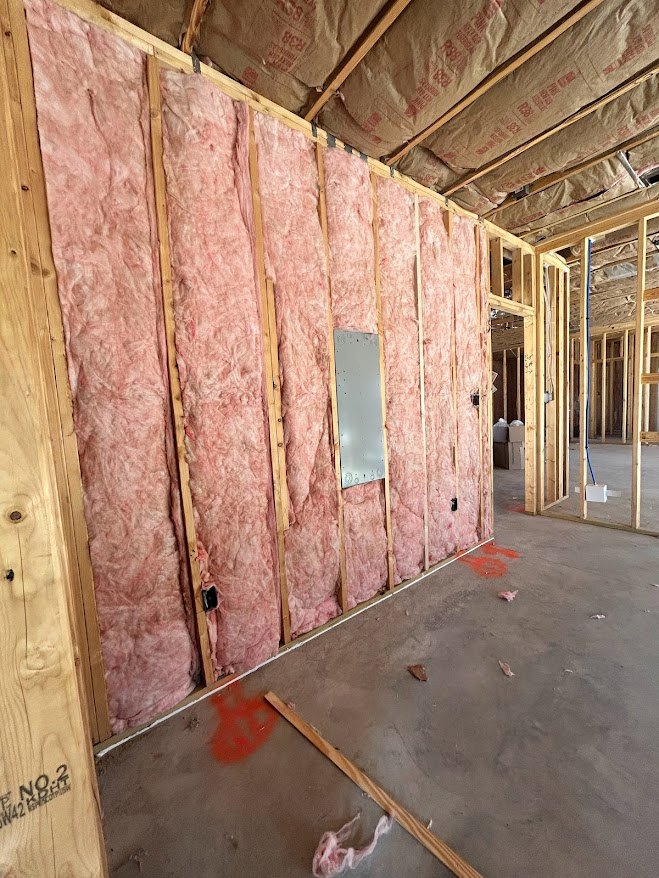 Room under construction with exposed wood beams and wall insulation, unfinished floor visible.