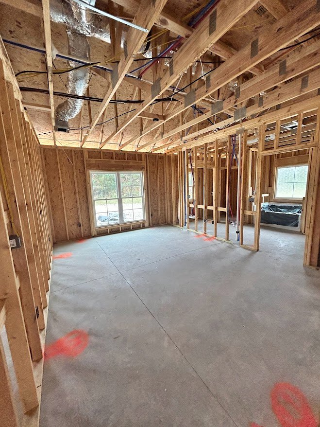 Concrete-floored room with exposed wood beams, grid window, red circles on floor, plastic bag on table, and visible building insulation