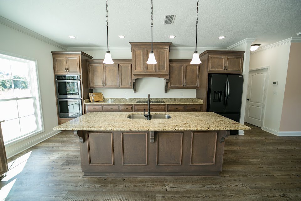 Spacious kitchen featuring a granite island with built-in sink and modern faucet, black refrigerator with glass door and matching handles, white cabinetry, and large window