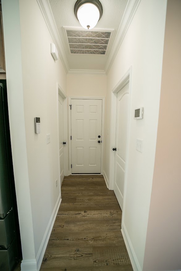 Hallway with light wood flooring, white paneled doors featuring black knobs, white walls, and crown molding