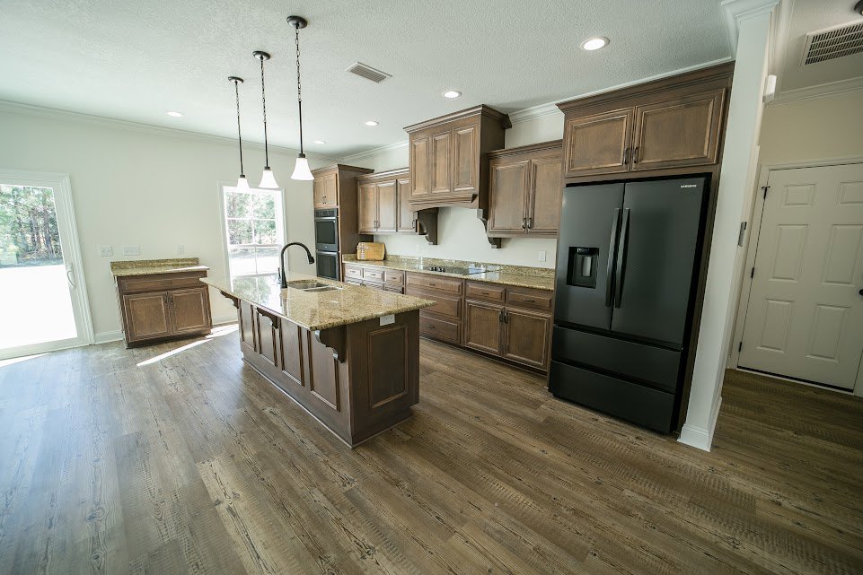 Kitchen with black double-door refrigerator, black island featuring built-in sink, wood flooring, white cabinetry with black hardware, pendant ceiling lights, and stone