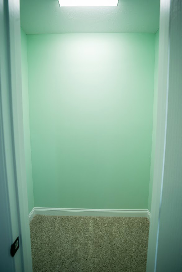 Wide hallway with light-colored walls, recessed ceiling light, and wall-mounted sconce; visible doorway leads to bathroom with tiled shower.
