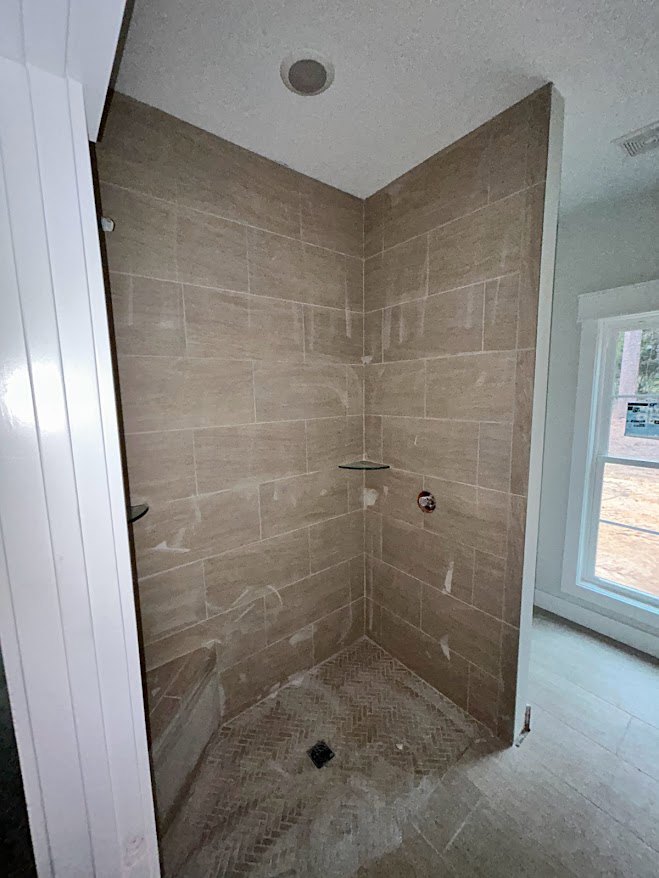 Walk-in shower with light gray tile floor, glass enclosure, white framed window, and white door visible in modern bathroom.