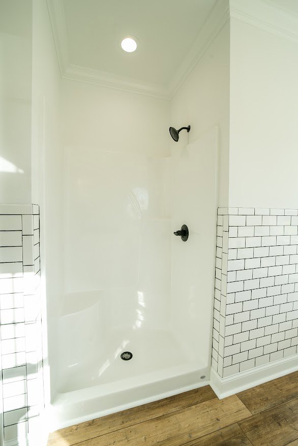 Walk-in shower with white subway tile walls featuring black grout lines, glass enclosure, and light gray floor tiles in a modern bathroom.