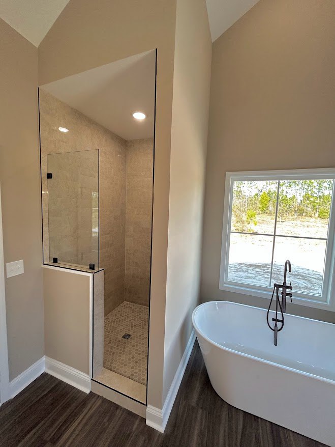 Bathroom with glass shower enclosure, white freestanding tub beneath window, chrome faucet, light tile walls, and modern fixtures.