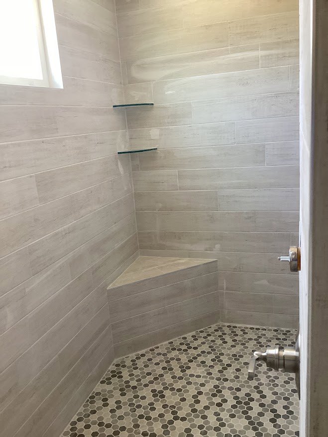 Shower featuring gray and black hexagon tile floor, white plaster walls, and a window providing natural light