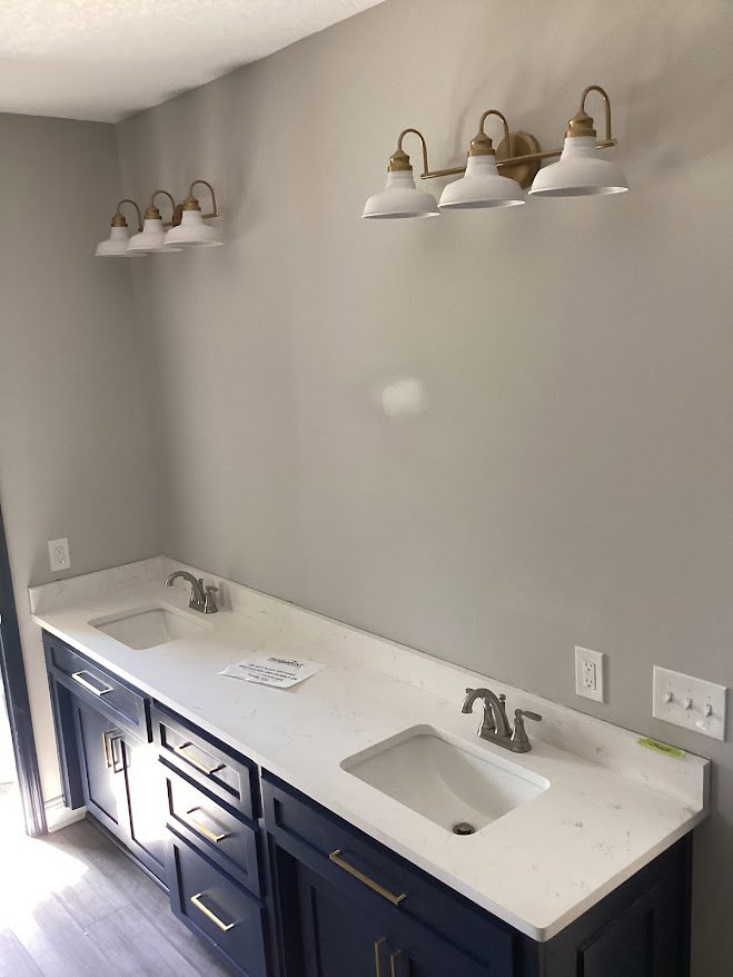 White countertop with integrated sink and silver faucet atop blue cabinetry, three-light fixture mounted above, tile backsplash and drawers visible in bathroom interior.