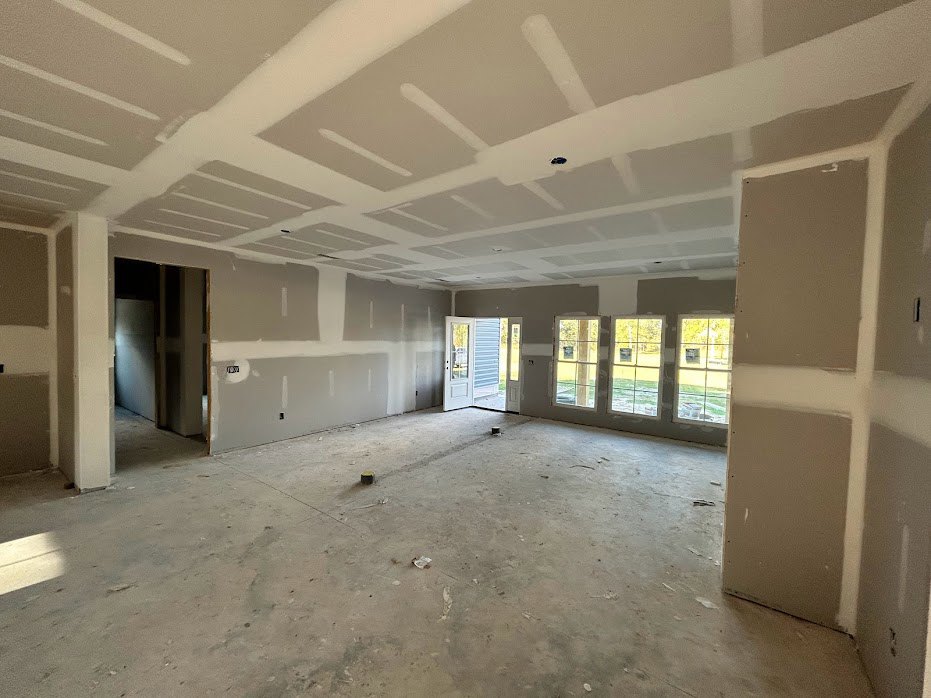 White-painted room with a row of windows, white plaster ceiling, glass-paneled door, and scattered objects on the floor.