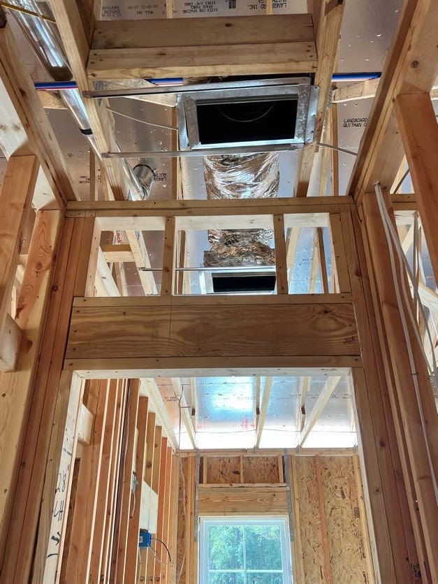 Exposed wood framing with visible ceiling ducts, white-framed window, and electrical wiring along unfinished wall