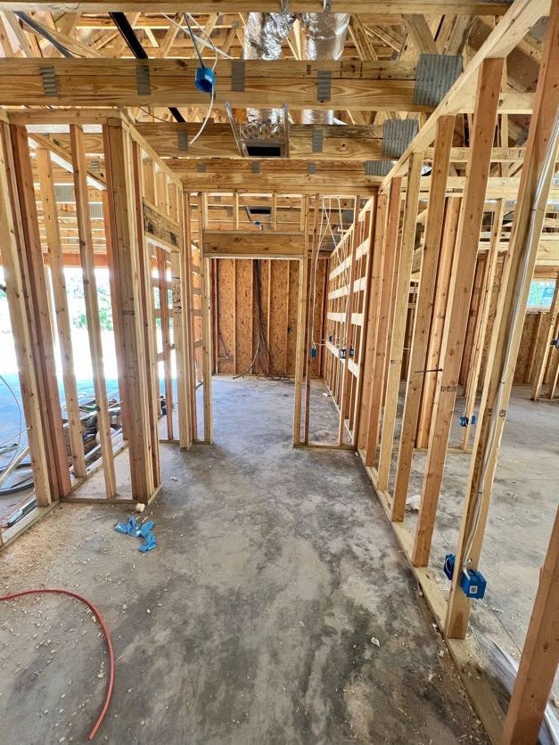 Exposed wood framing and beams inside a partially constructed home, red hose lying on concrete floor, visible electrical cable, unfinished walls, and grey surface detail