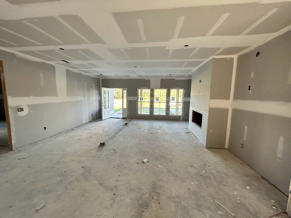 Spacious room with white plaster walls, row of large windows with white frames, ceiling fan mounted on smooth ceiling, concrete floor, open door leading to grassy yard