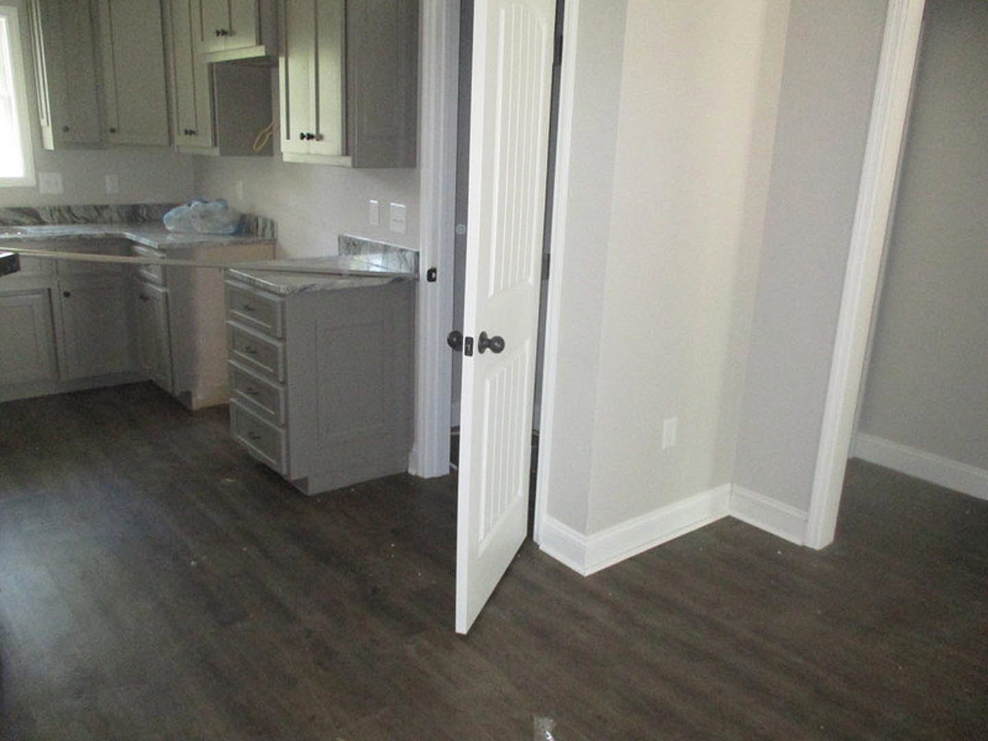 White kitchen cabinets with drawers and silver handles, wood flooring, stone countertop, partially open white door leading to adjacent room