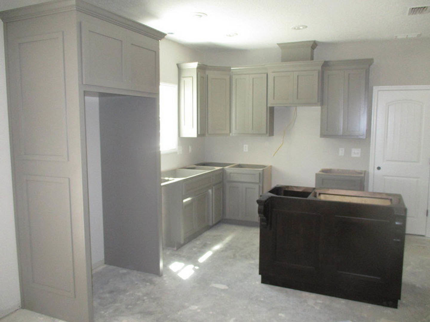 Modern kitchen featuring white cabinetry, black island with waterfall countertop, tile backsplash, stainless steel sink, and light wood flooring