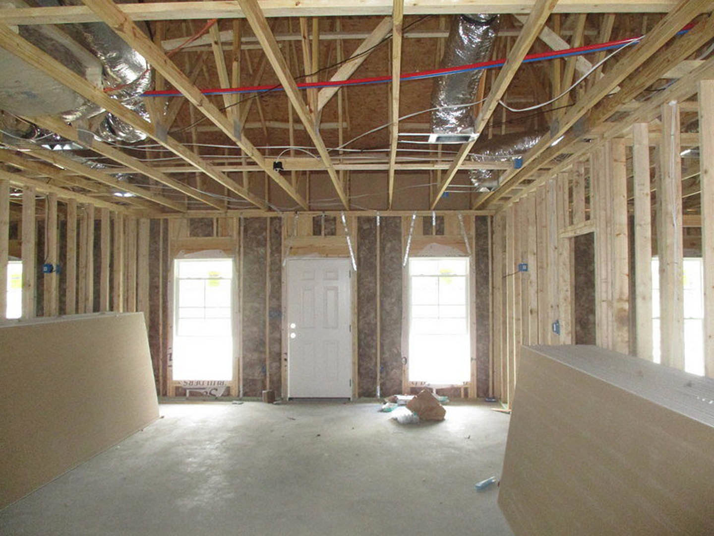 Open room with exposed wood ceiling beams, white plaster walls, large window featuring a yellow post-it note, and a white door illuminated by natural daylight.