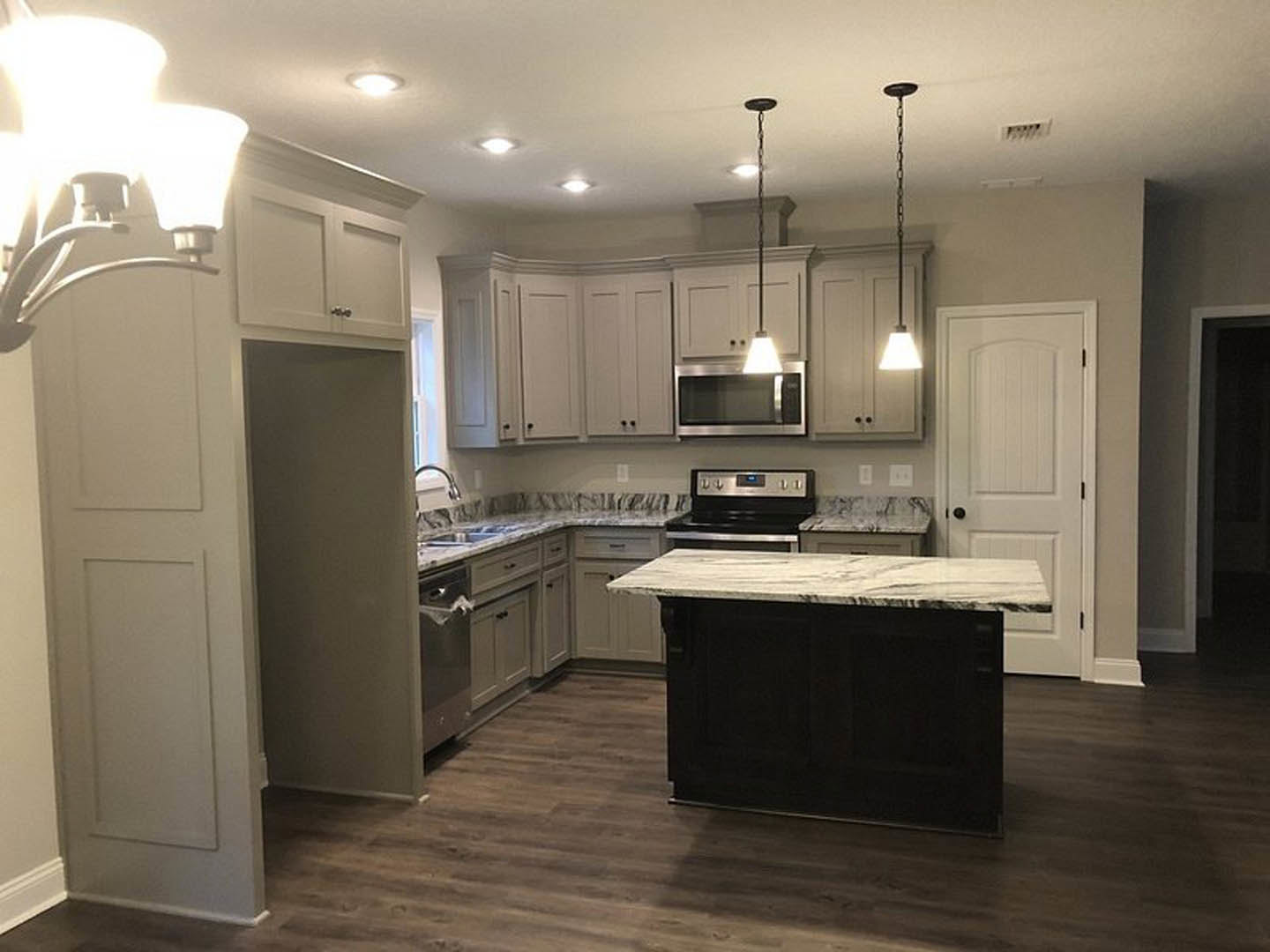Kitchen with marble countertops, wood flooring, white cabinetry, stainless steel appliances, kitchen island with marble top, modern light fixture with white shade