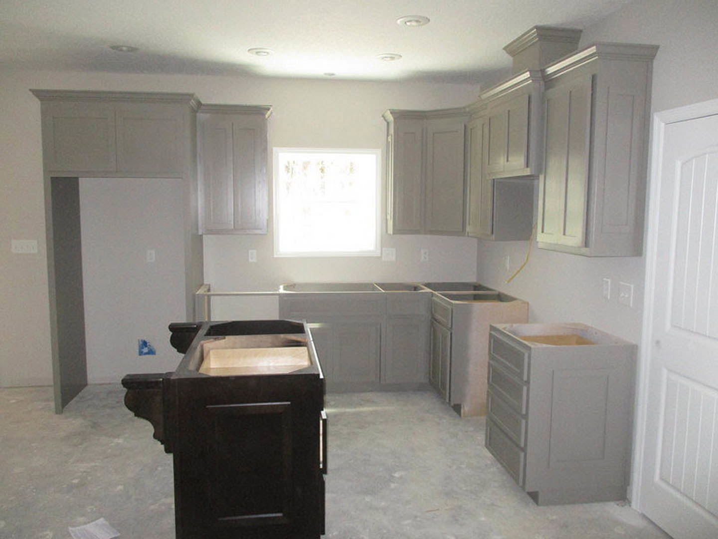 Gray shaker cabinets with brushed nickel hardware, white quartz countertops, a white square window letting in natural light, black wooden cabinet with open shelf, white lower
