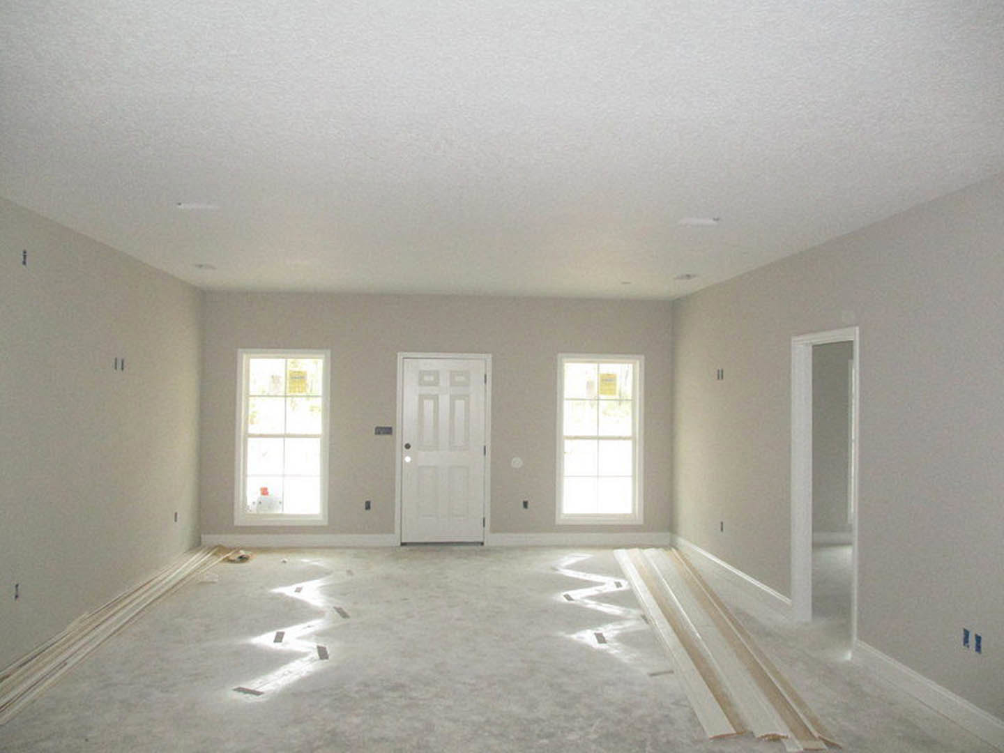 White-walled room featuring a white door with adjacent light fixture, white-framed window, and smooth white flooring